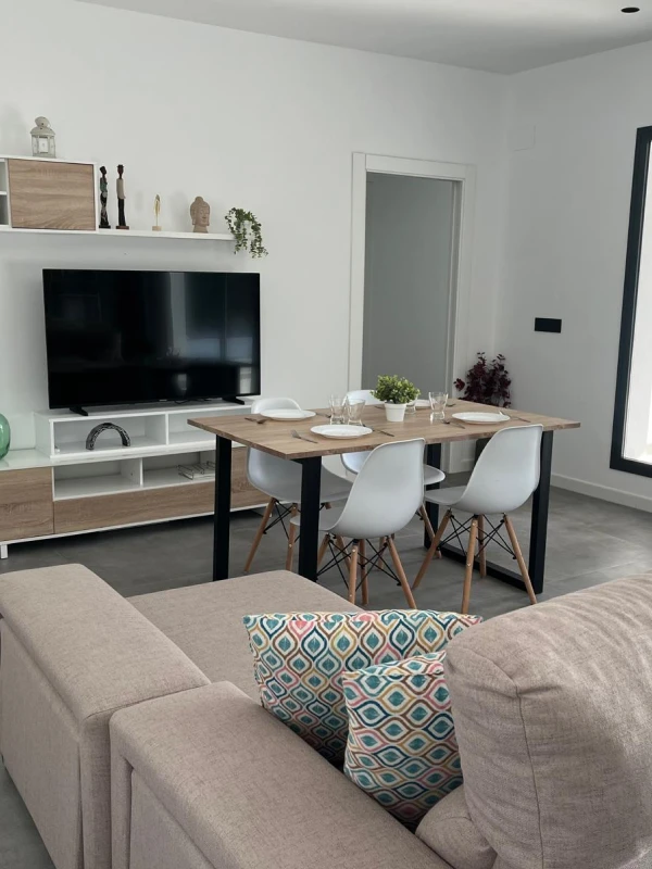 Sala de estar con sofá gris y mesa de comedor con cuatro sillas blancas