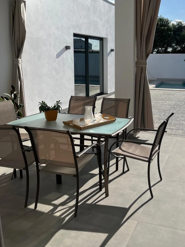 Mesa de comedor al aire libre con sillas de metal y vidrio en un patio moderno con piscina