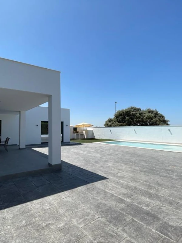 Imagen de una moderna piscina y área de descanso al aire libre con baldosas grises y una estructura de sombra blanca.