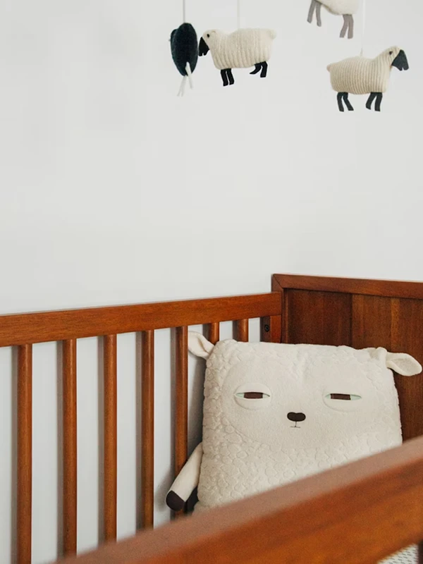 cuna de madera con cojín de cordero y móviles de corderos