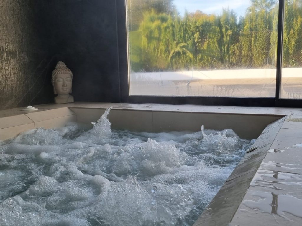 Foto de un jacuzzi con agua burbujeante en una villa de lujo con una estatua de Buda en el fondo